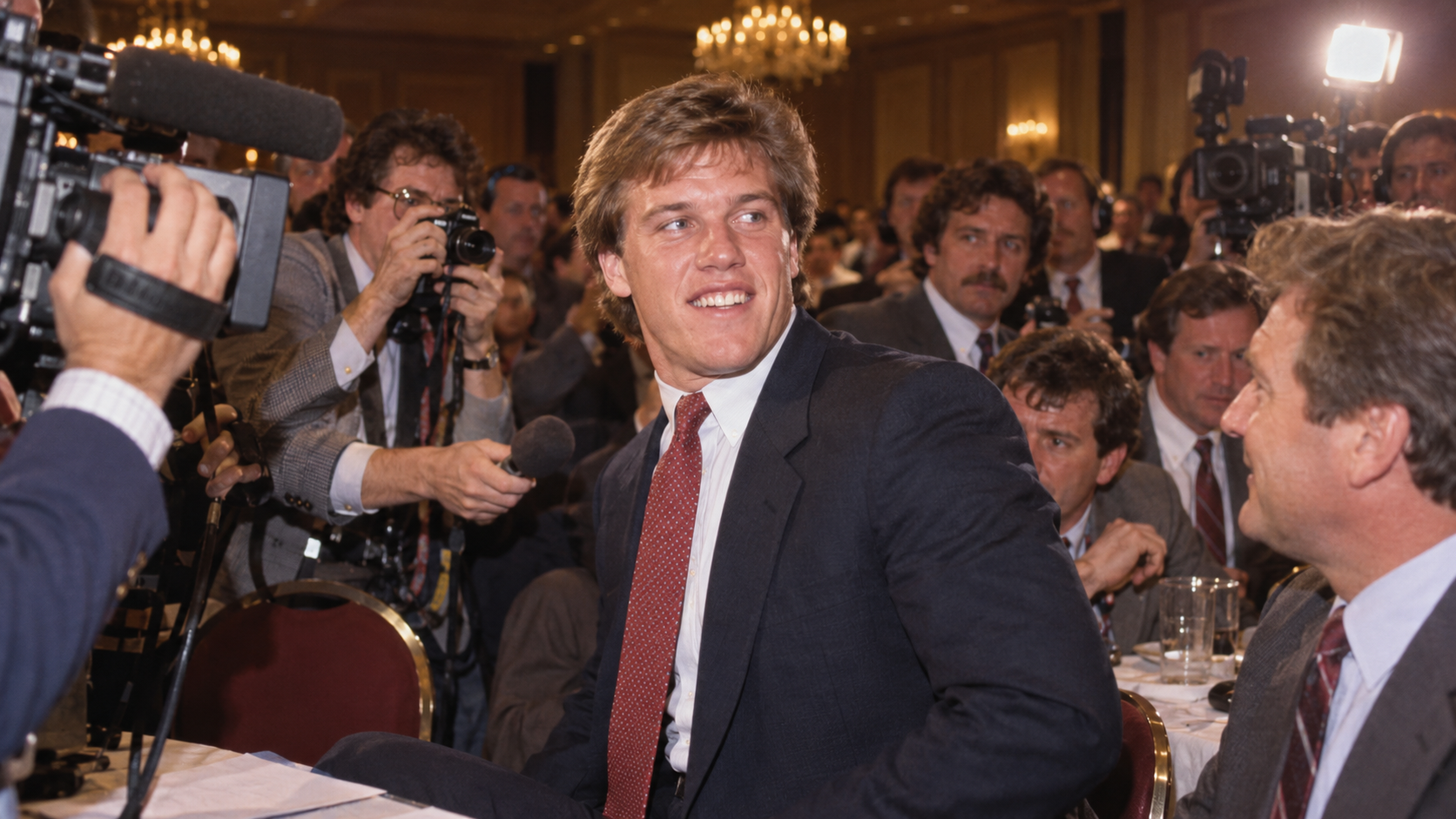 Photorealistic historical reconstruction of John Elway surrounded by reporters during the 1983 NFL draft.