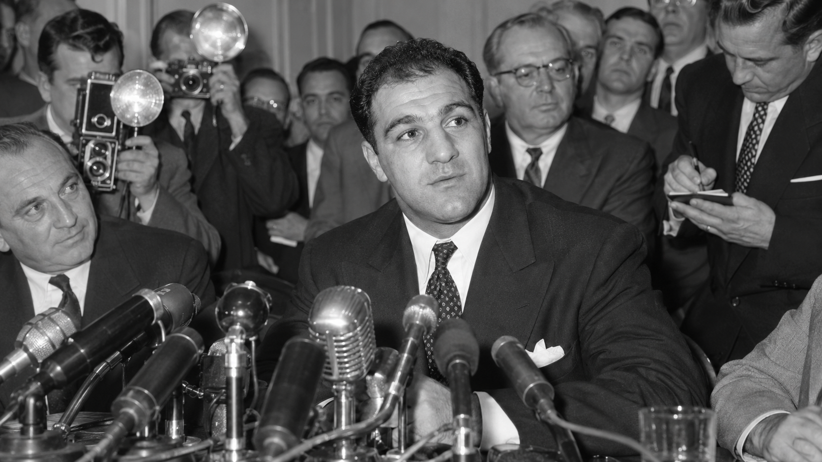 Photorealistic historical reconstruction of Rocky Marciano announcing his retirement at a 1956 press conference.