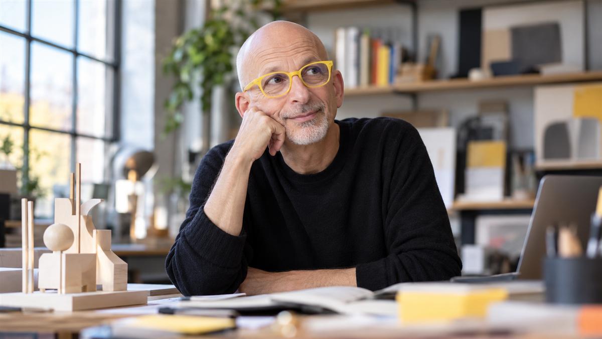AI-generated editorial portrait of Seth Godin weighing a small experimental launch in a creative studio