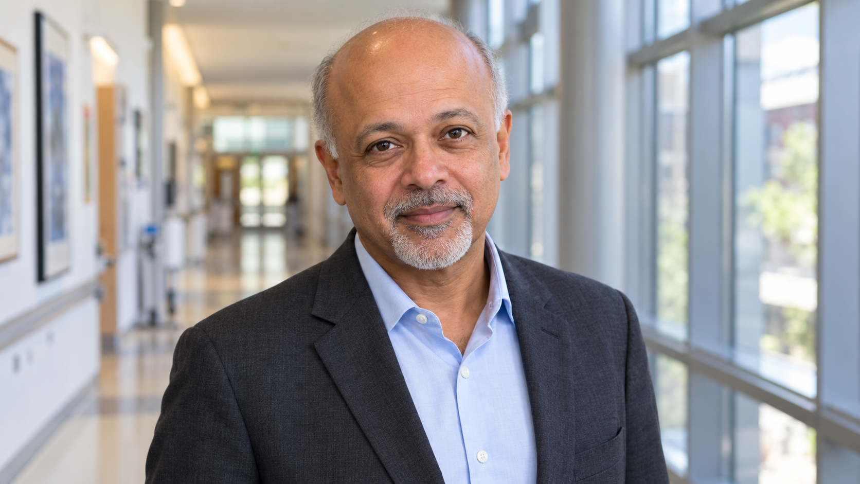 AI-generated realistic portrait of Abraham Verghese in a recreated university hospital teaching corridor, circa 2016.