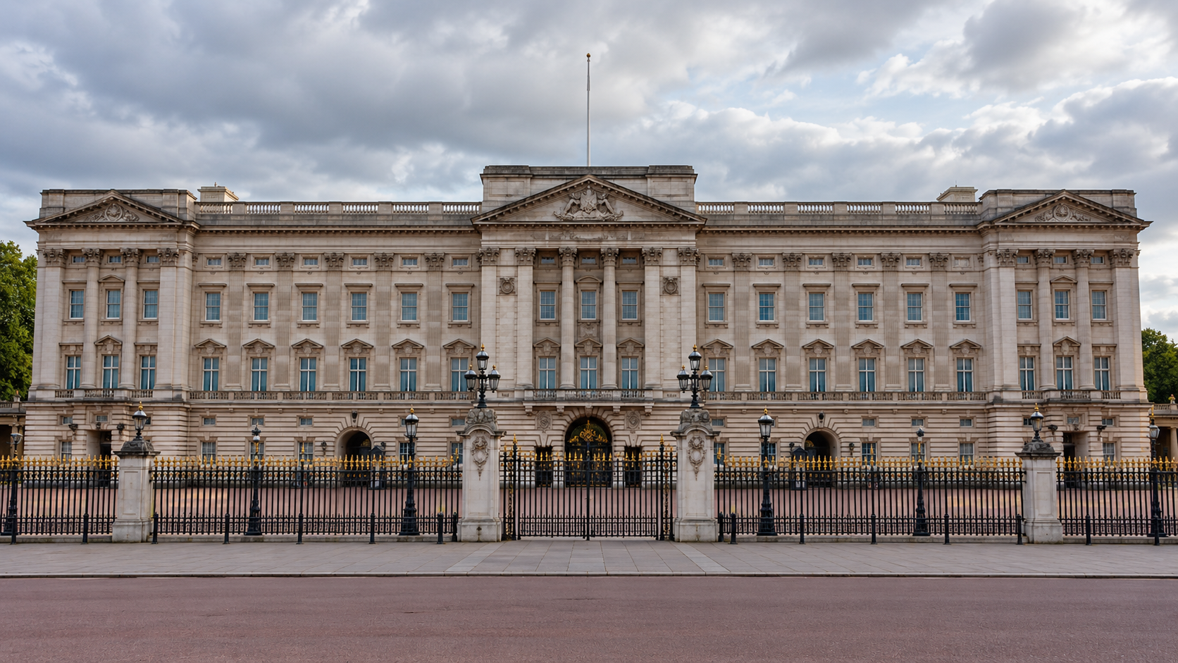 The pale stone facade and central balcony of Buckingham Palace behind iron railings