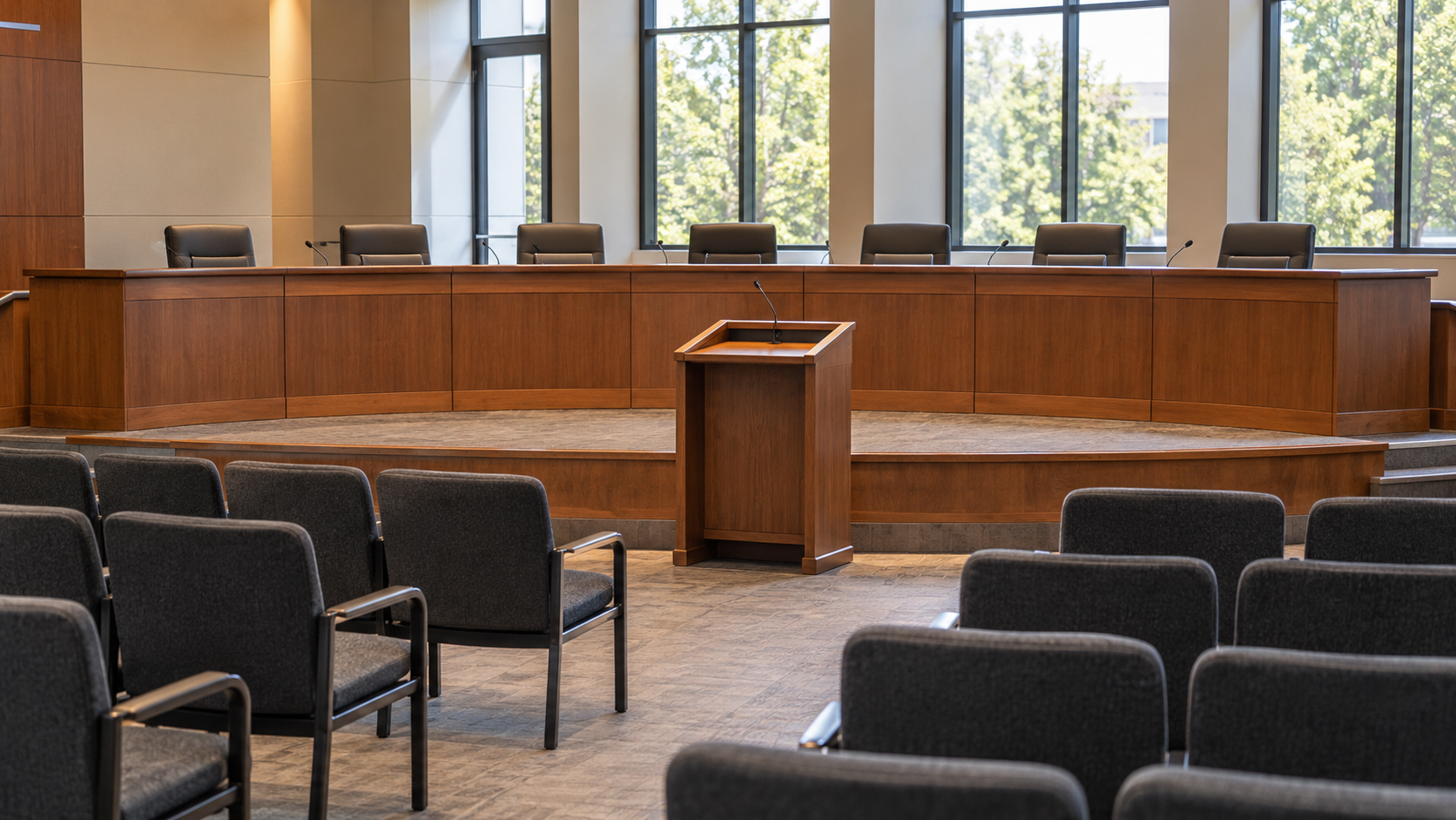 An empty city-council chamber with a curved wooden dais and public-comment lectern