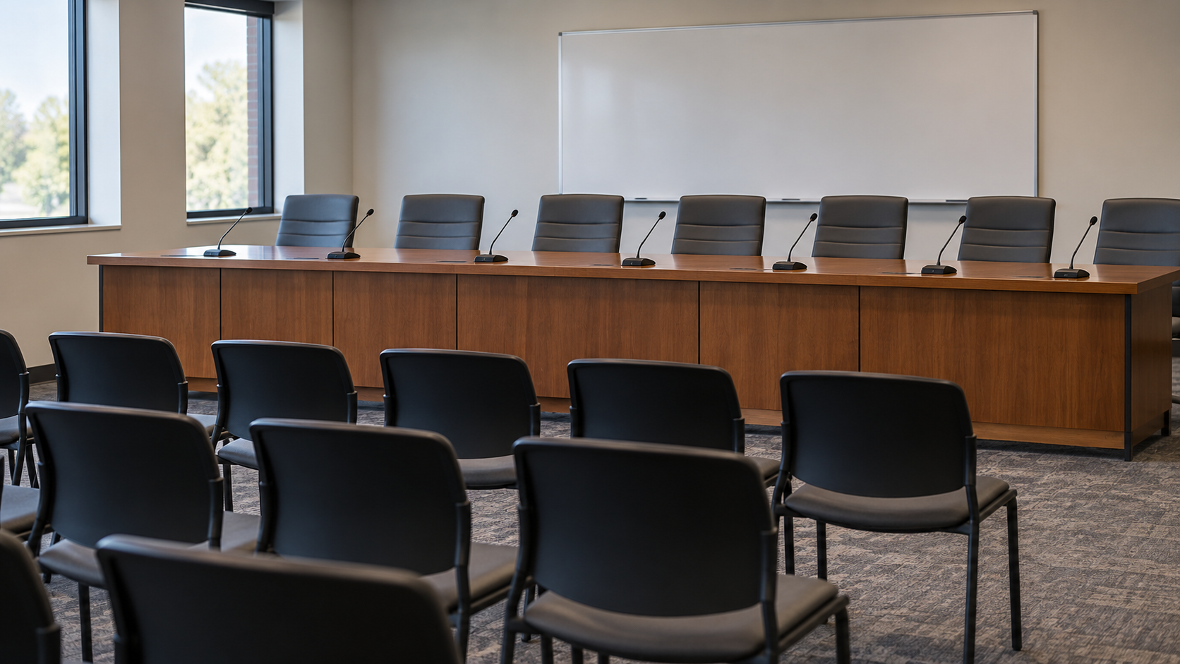 An empty school-district meeting room with a long table, microphones, and audience chairs