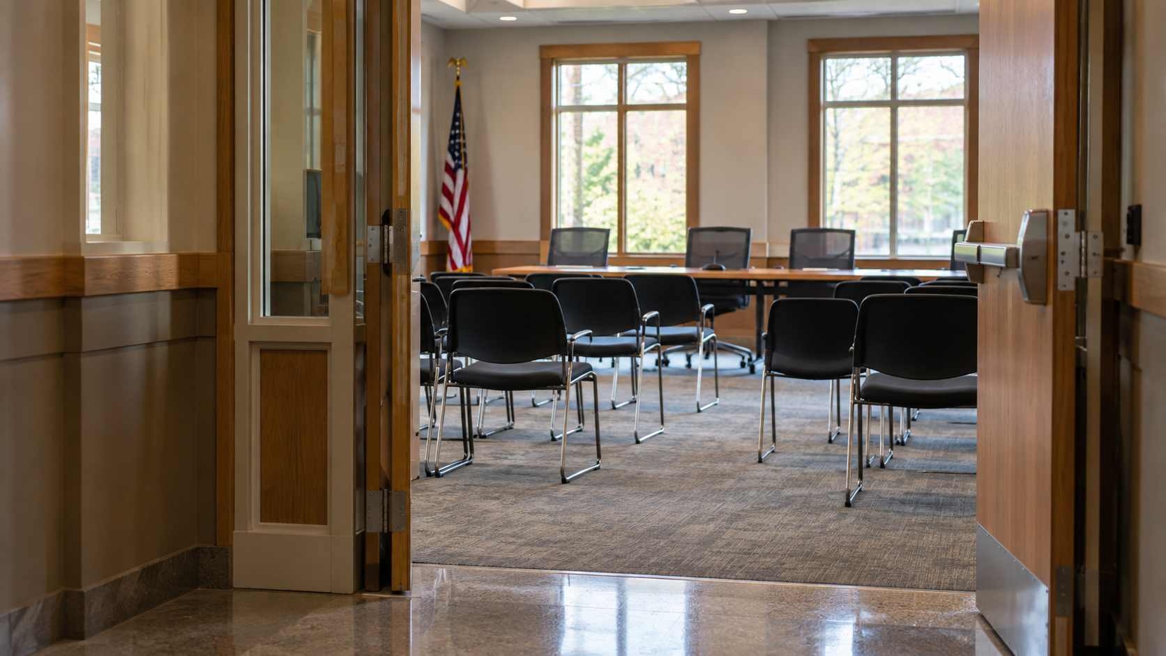 An open doorway leading into a community meeting room with empty chairs and daylight windows