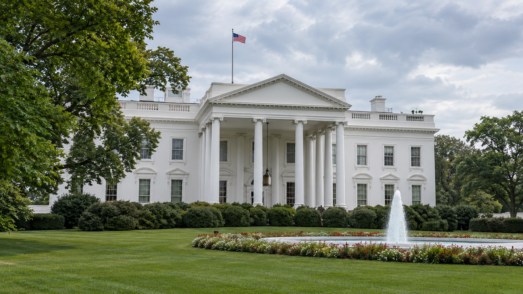 The White House North Portico behind a lawn and fountain under a cloudy sky.