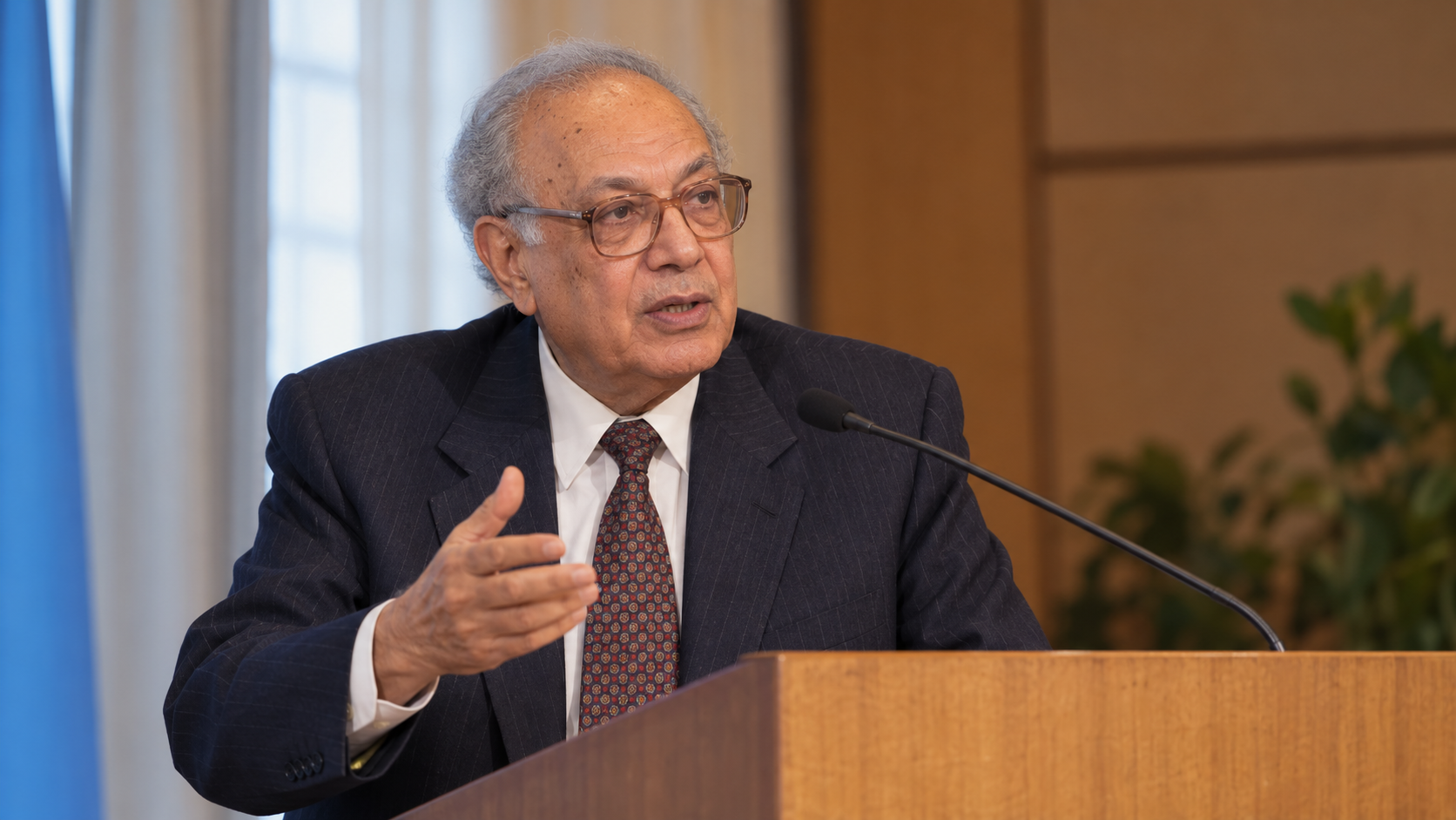 Mahmoud F. Fathalla in a global maternal-health conference room with a simple lectern and warm natural light