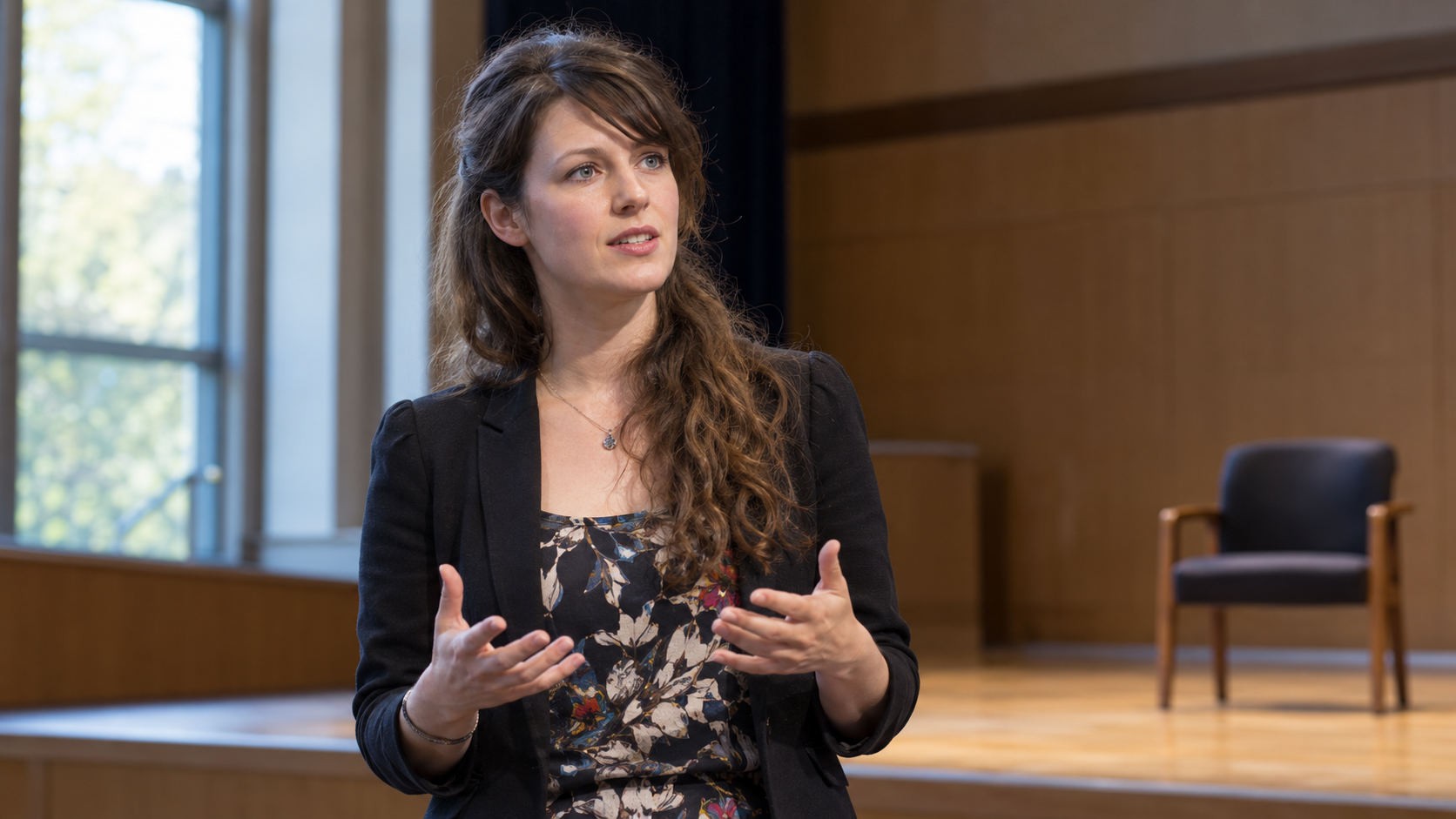 Eleanor Longden in a quiet lecture hall with a single empty chair and understated stage lighting