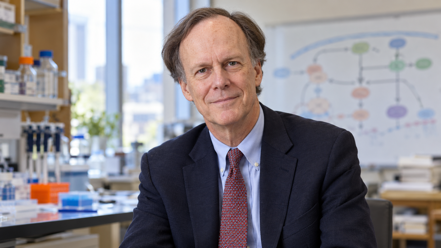 William G. Kaelin Jr. in a cancer-biology laboratory office with a simple protein pathway diagram blurred behind him