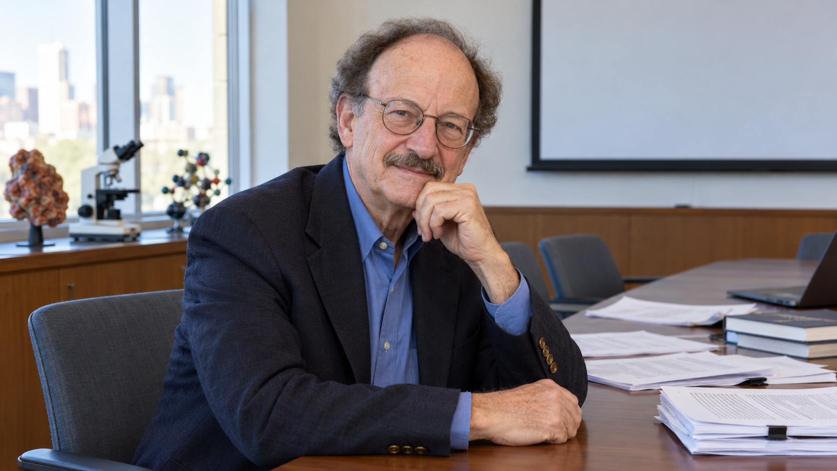 Harold E. Varmus in a cancer-research seminar room with manuscript pages and an empty projection screen