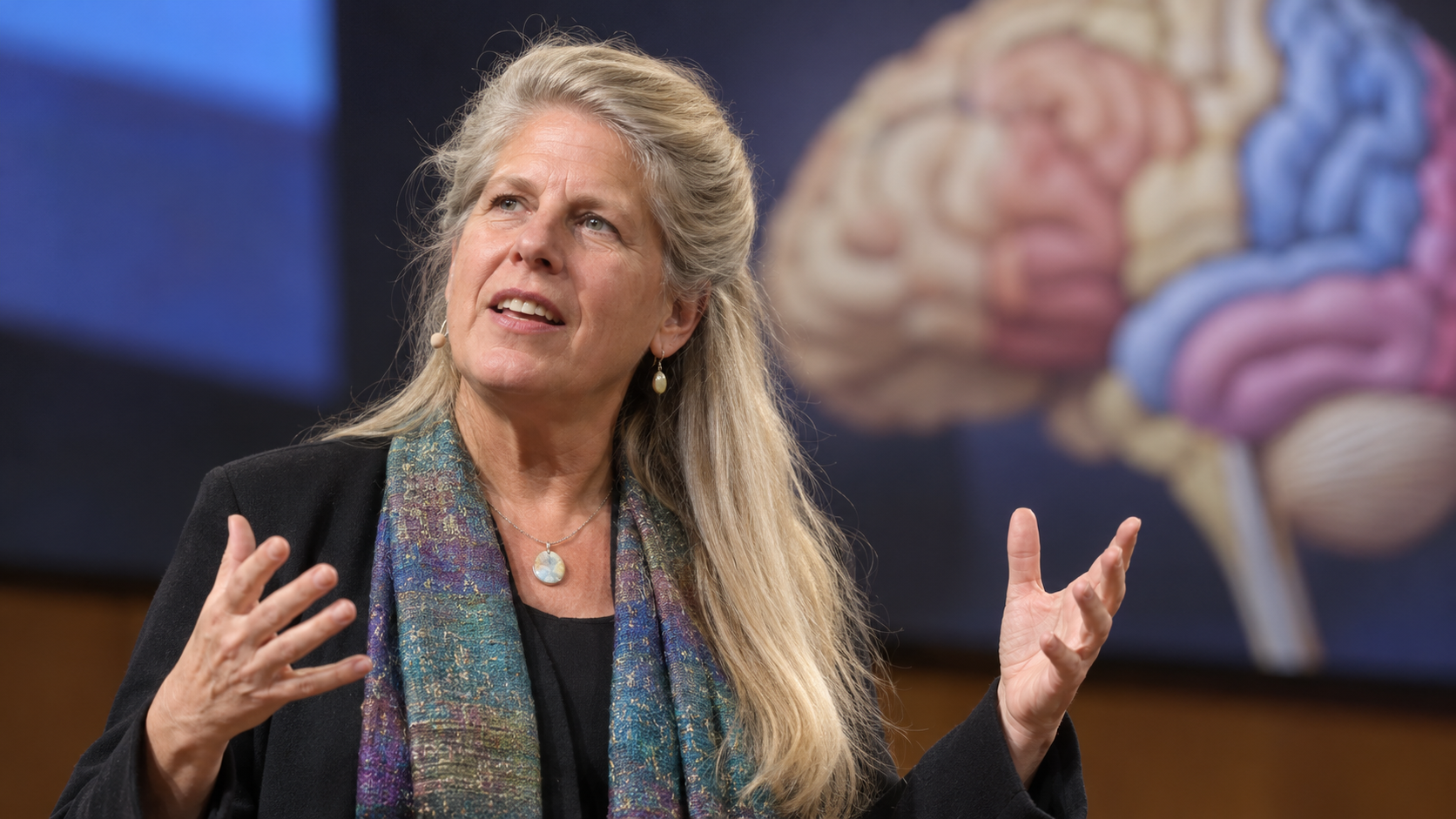 Jill Bolte Taylor in a neuroscience lecture stage with a softly blurred brain model
