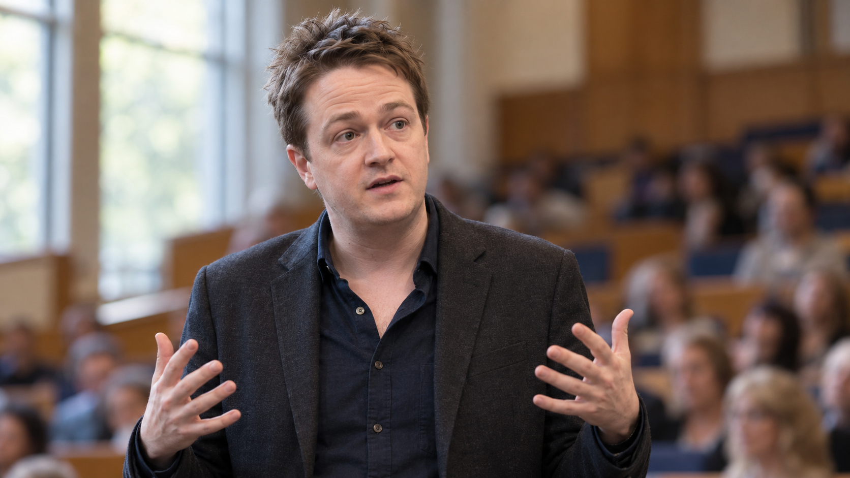 Johann Hari in a public-health lecture hall with audience seats softly out of focus
